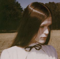 a woman with long brown hair standing in a field