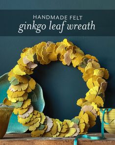 a wreath made out of yellow leaves on top of a wooden table next to a cup and saucer