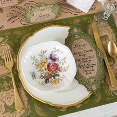 a place setting with gold and white plates, silverware and napkins on a green table cloth