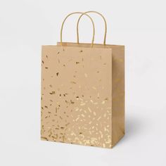 a brown paper bag with gold confetti on the handle and handles, against a white background