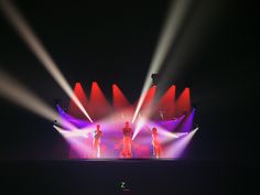 three people standing on stage with their backs turned to the side and lights behind them