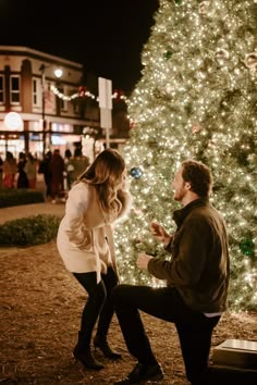 a man kneeling down next to a woman near a christmas tree