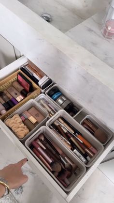 an open drawer with various cosmetics and makeup products in it on a marble countertop