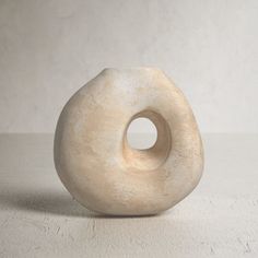 a white vase sitting on top of a table next to a wall with a hole in it