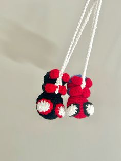 two crocheted red and black stuffed animals hanging from white strings on a gray background