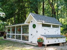 a white chicken coop sitting in the middle of a yard with potted plants on it