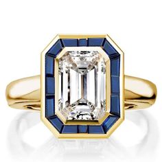 an emerald and blue sapphire engagement ring in yellow gold with diamonds on the sides, set against a white background