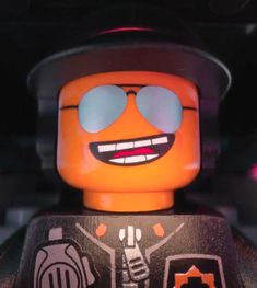 a lego man wearing sunglasses and a hat with his eyes closed, standing in front of a dark background