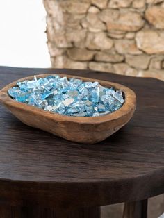 a wooden bowl filled with blue sea glass on top of a table next to a stone wall