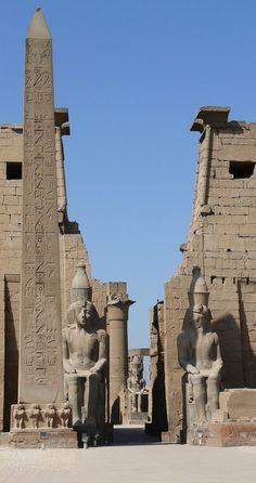 two large statues in front of some very tall buildings with writing on the side of them