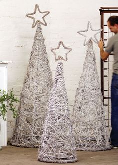 a man standing next to three wire christmas trees