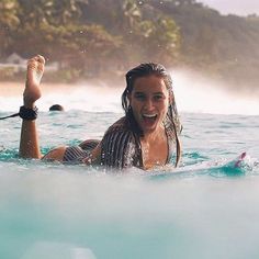 a woman in the water with headphones on, holding her surfboard and smiling