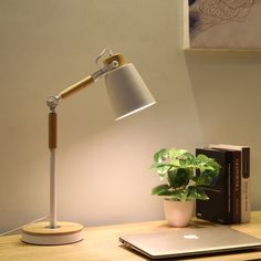 a desk lamp sitting on top of a wooden table next to a book and laptop