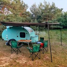 an old camper trailer is set up in the grass with two chairs and a table underneath it