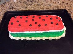 a watermelon cake with black dots on it sitting on a baking sheet in the kitchen