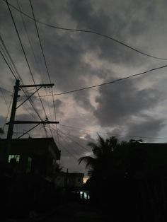 the sky is dark and cloudy with power lines in front of houses, palm trees, and telephone poles