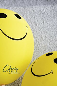 two yellow balloons with smiley faces on them sitting on the floor next to each other