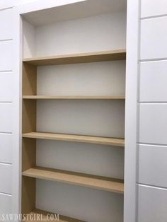 an empty bookcase in the corner of a room with white walls and wood shelves