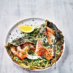 a white plate topped with salmon and spinach covered in sauce next to a fork