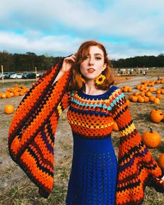 a woman in an orange and blue crochet dress standing next to pumpkins