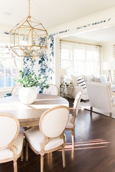 a dining room table with white chairs and a chandelier hanging from the ceiling