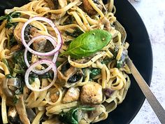 pasta with mushrooms, spinach and onions in a black bowl on a white table