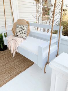 a white porch swing with pillows hanging from it's sides and a rug on the floor