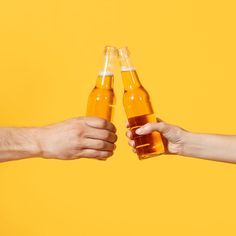 two people toasting with beer in front of an orange background and one holding the other's hand