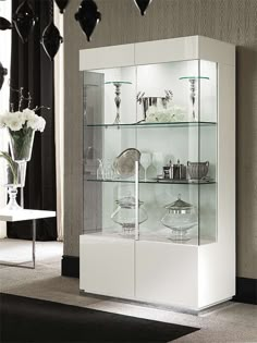 a white display cabinet with glass shelves and vases on the top, in a living room