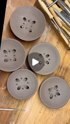 four gray bowls sitting on top of a wooden table next to bamboo sticks and paintbrushes