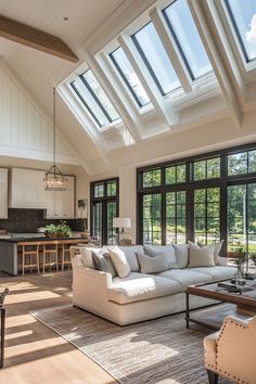 a living room filled with lots of furniture under a skylight in front of windows