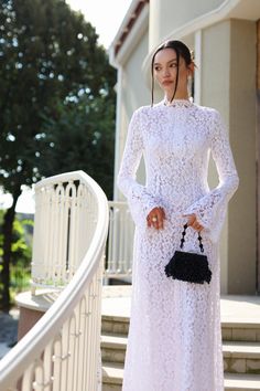 a woman in a white dress is standing on the steps with her purse and looking at the camera