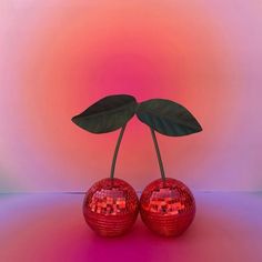 two shiny red apples with green leaves in front of a pink and blue background,