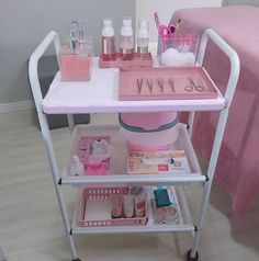 a pink cart filled with personal care items on top of a wooden floor next to a bed