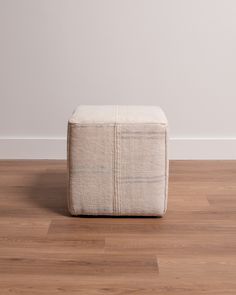 a square footstool sitting on top of a hard wood floor next to a white wall