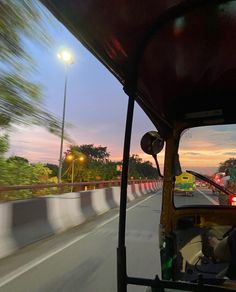 the view from inside a vehicle driving on a highway at dusk or dawn, with trees and street lights in the background