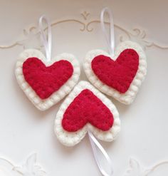 three crocheted heart ornaments hanging on a white table