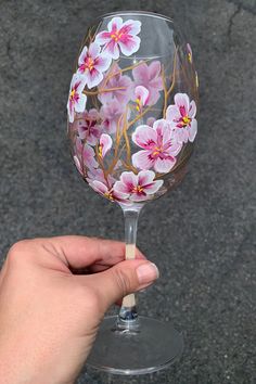 a hand holding a wine glass with pink flowers painted on the outside and inside it