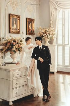 a man and woman posing for a photo in front of a dresser with flowers on it