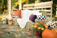 pumpkins, hay bales and flowers on the ground in front of a wooden bench