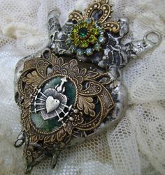 an ornate brooch with a heart on it sitting on a lace tablecloth covered surface