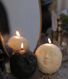 two candles sitting next to each other with faces on them in front of a mirror