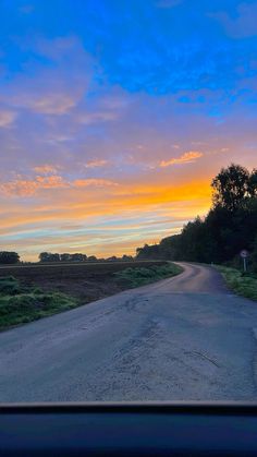 the sun is setting on an empty road near some trees and bushes in the distance