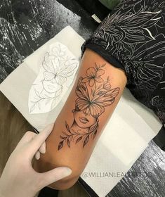 a woman's arm with flowers on it and a black ink drawing behind her