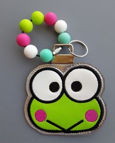 a key chain with a green frog face on it and a beaded necklace attached to it