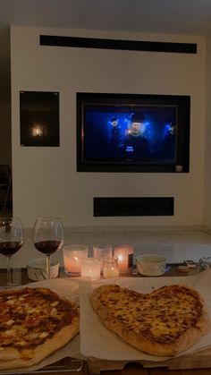 two pizzas sitting on top of a table next to wine glasses and candle holders