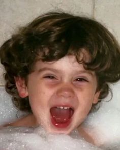 a little boy that is in the bathtub with soap on his face and mouth