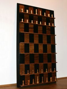 a wooden shelf with chess pieces on it in front of a white wall and wood floor