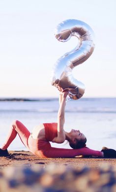 a woman laying on the beach with an inflatable number 2 balloon attached to her head