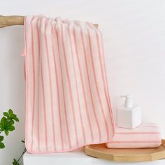 a pink towel sitting on top of a wooden shelf next to a white vase with a green plant